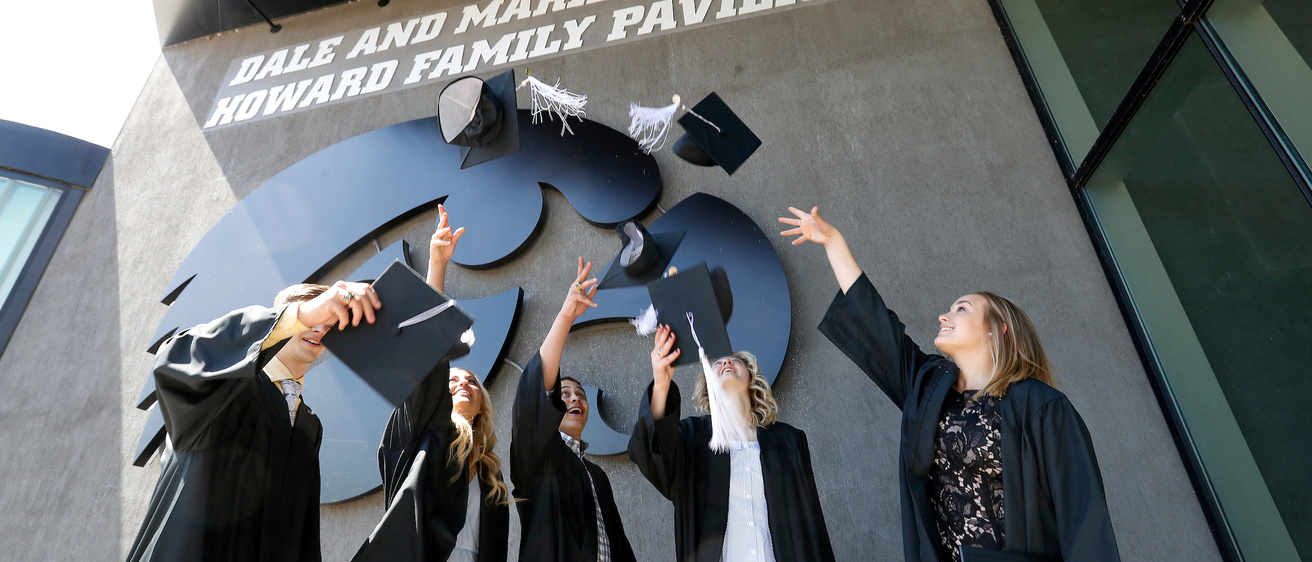 Five graduates toss their hats in the air